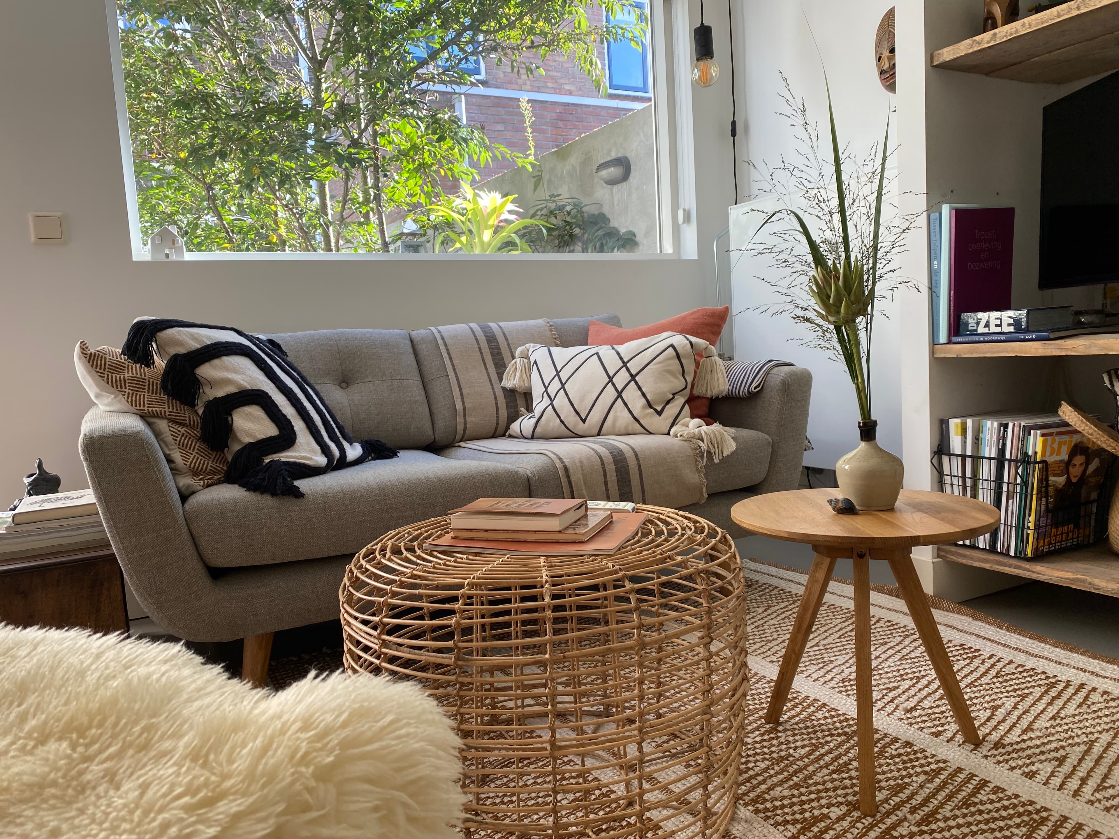 Gemütliches Wohnzimmer im Romantic Wellness B&B mit grauem Sofa, geflochtenem Couchtisch, Büchern und Blick auf den grünen Innenhof.