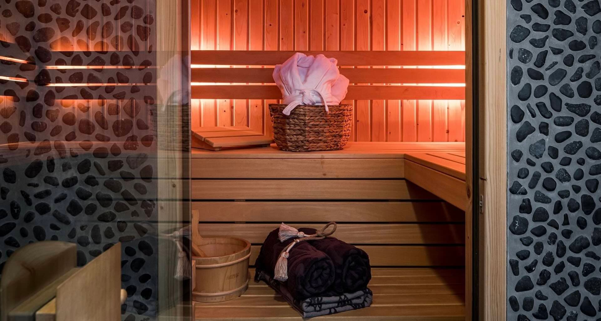 Warm beleuchtete private Sauna mit Holzbänken, Bademänteln, dunklen Handtüchern und einem Holzeimer im Romantic Wellness B&B.