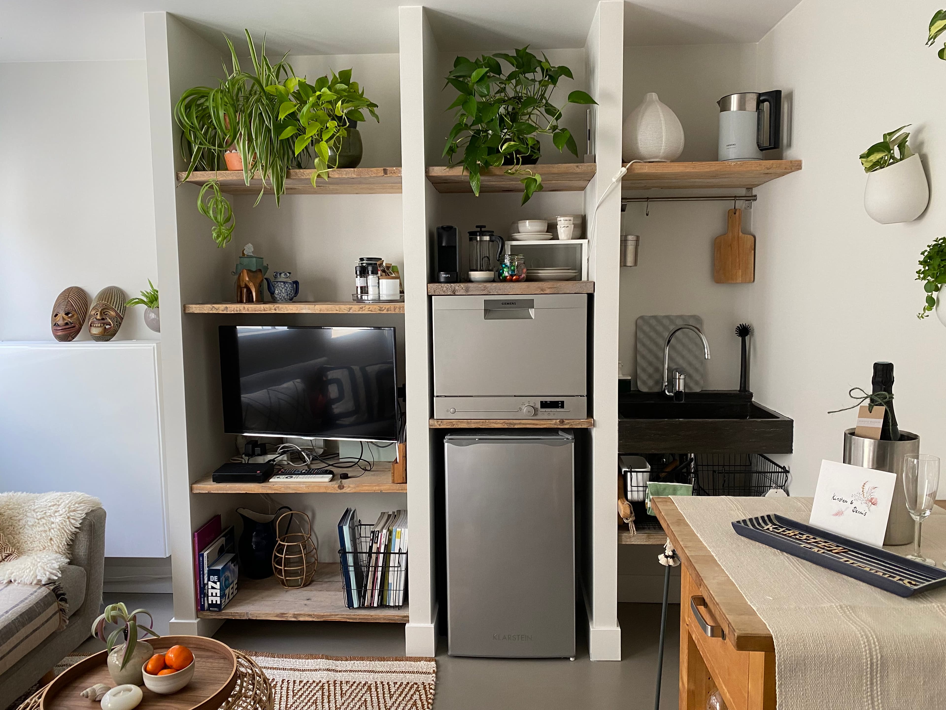 Kompakte Gästeküche mit Spüle, Kaffeemaschine, Kühlschrank, Fernseher und bepflanzten Einbauregalen im Romantic Wellness B&B.