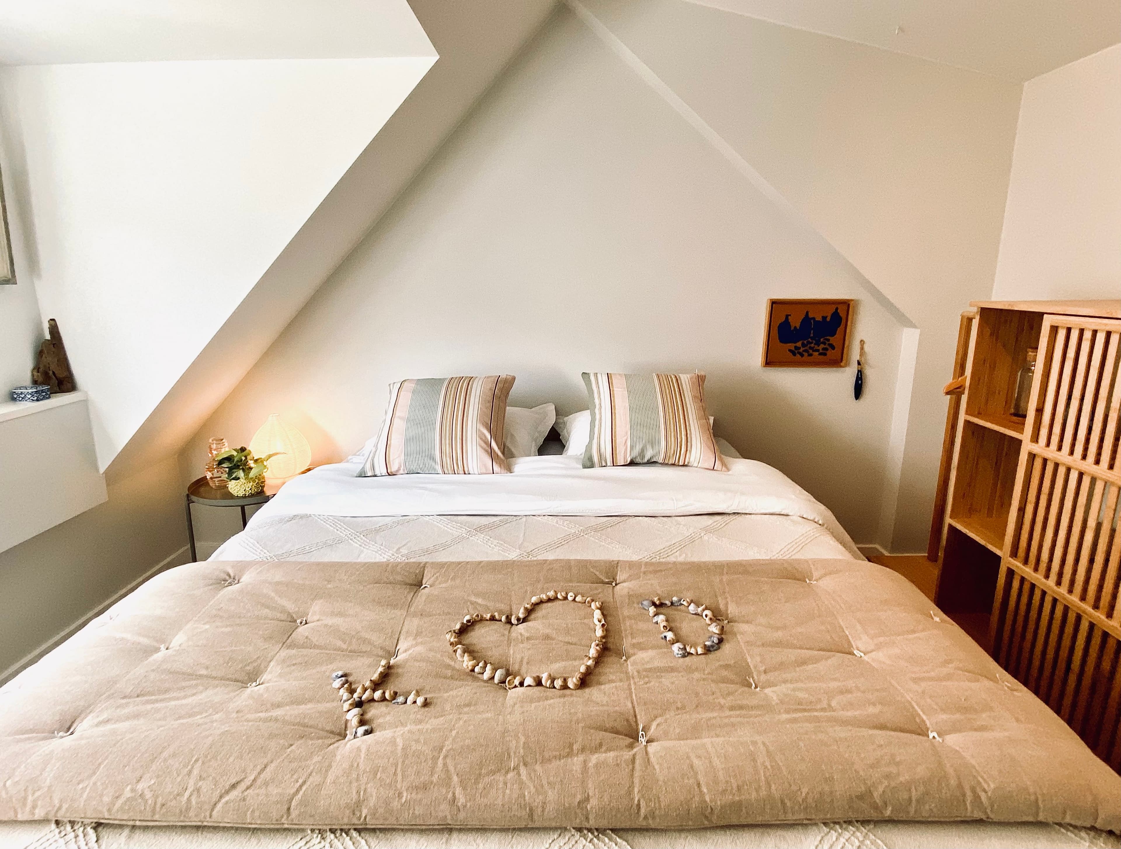 Ruhiges Schlafzimmer im Dachgeschoss des Romantic Wellness B&B mit Queensize-Bett, gestreiften Kissen und Muscheln, die LOVE bilden.