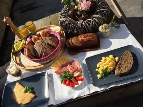Frühstückstisch im Romantic Wellness B&B mit warmem Brot, Käse, Aufschnitt, Eiern, Orangensaft und Blumen.