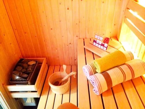 Private Holzsauna im Romantic Wellness B&B mit Bänken, Ofensteinen, einem Eimer und ordentlich gerollten Handtüchern.