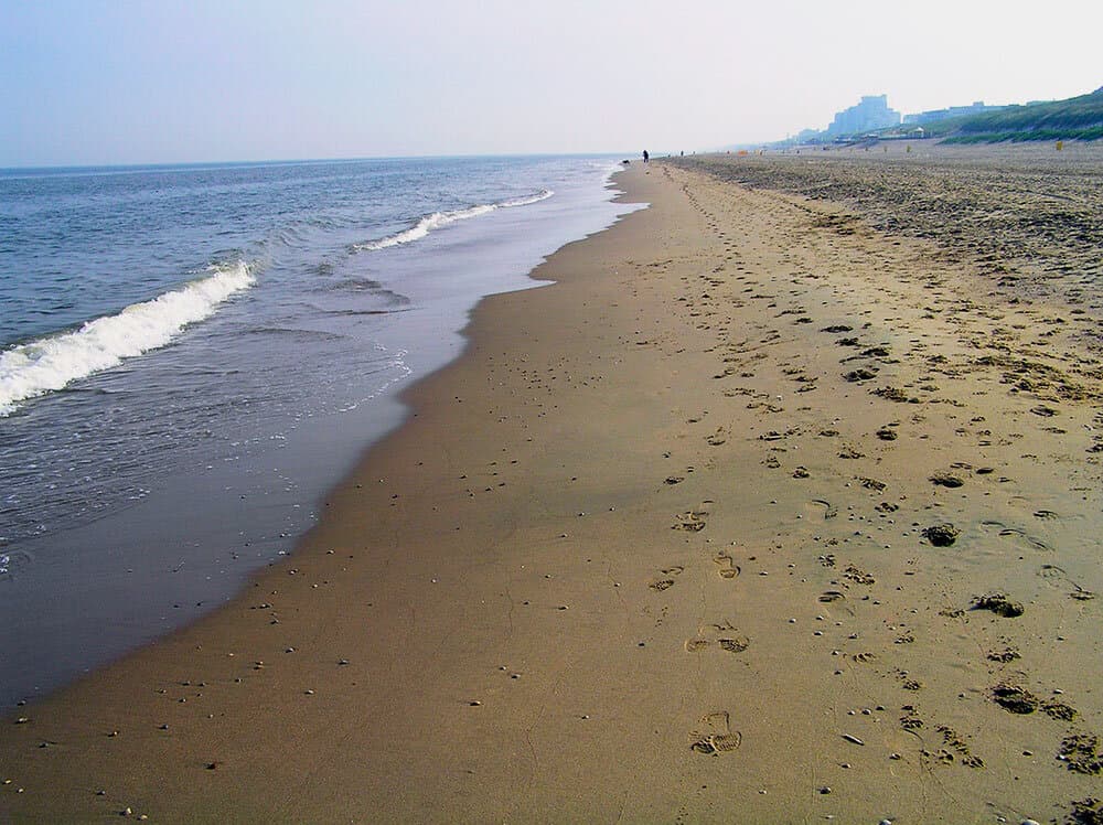 Wide sandy beach at Noordwijk with footprints along the North Sea shoreline and dunes in the distance.