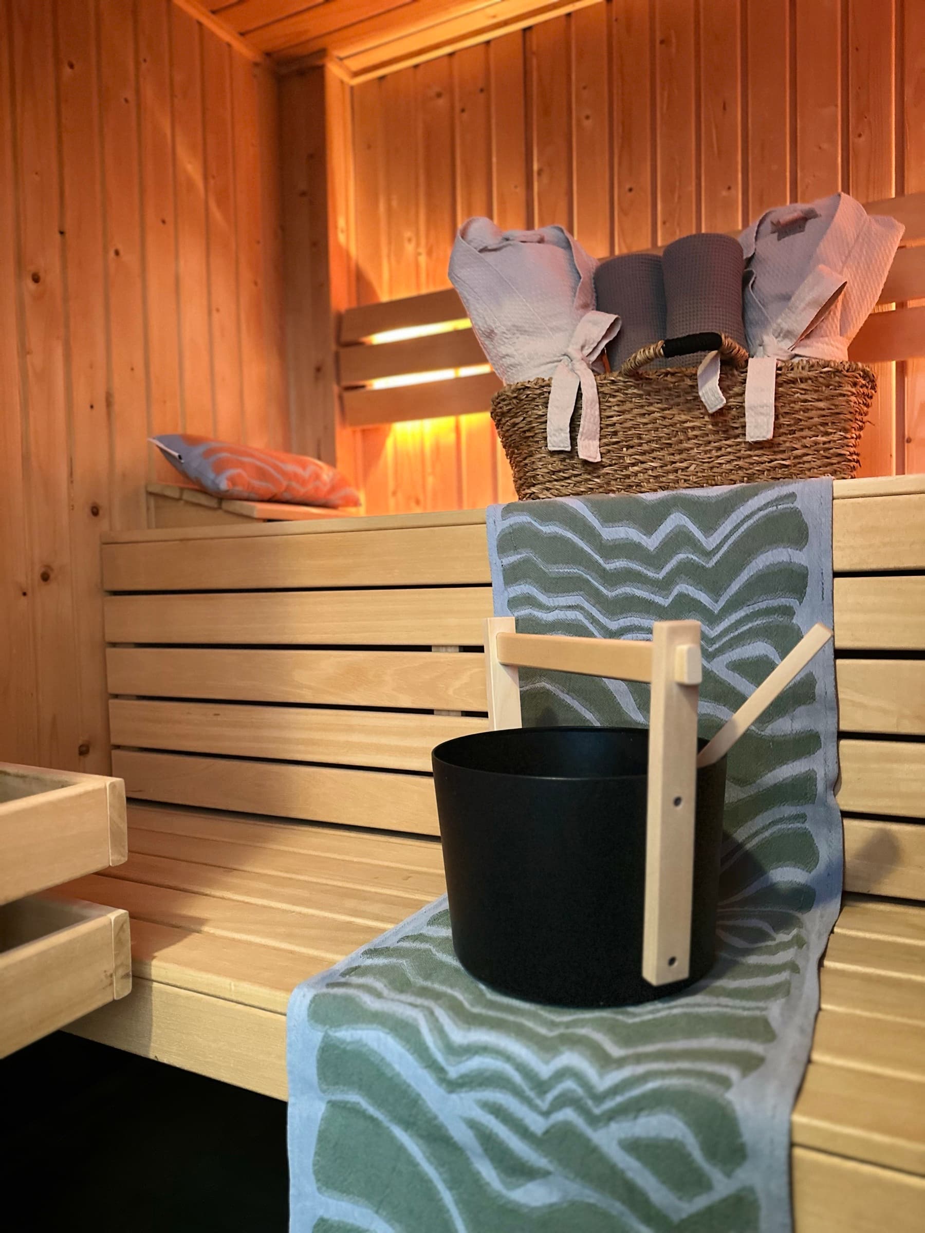 Warm private sauna at Romantic Wellness B&B in Noordwijk, with wooden benches, two bathrobes, green towels and a black sauna bucket.